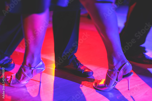 Dancing shoes of a couple, couples dancing traditional latin argentinian dance milonga in the ballroom, tango salsa bachata kizomba lesson, festival on a wooden floor, purple, red and violet lights