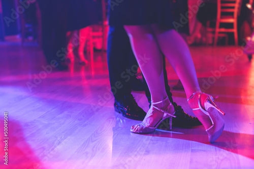 Dancing shoes of a couple, couples dancing traditional latin argentinian dance milonga in the ballroom, tango salsa bachata kizomba lesson, festival on a wooden floor, purple, red and violet lights