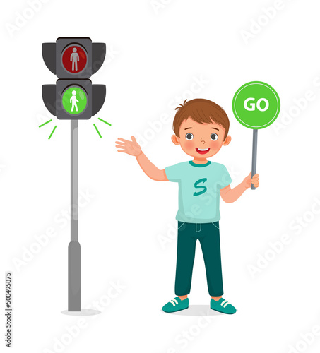 cute little boy holding go sign near pedestrian traffic light with indicator green light on