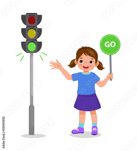 cute little girl holding go sign board showing traffic light indicator green light on