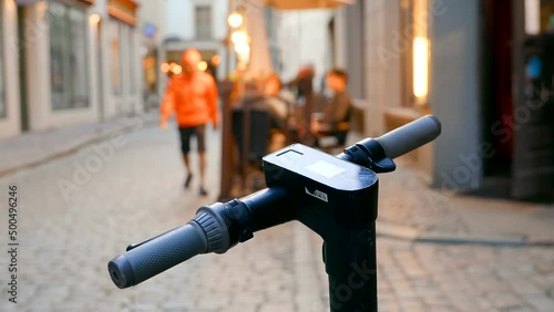 Close up of electric scooter handle against night city center and restaurant