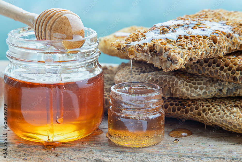 Close-up of Delicious honey dripping from Fresh honeycombs on Glass jar with Wooden honey dipper stick on old wooden table. Healthy organic natura honey, space for text, Selective focus. Close-up of Delicious honey dripping from Fresh honeycombs on Glass jar with Wooden honey dipper stick on old wooden table. Healthy organic natura honey, space for text, Selective focus.