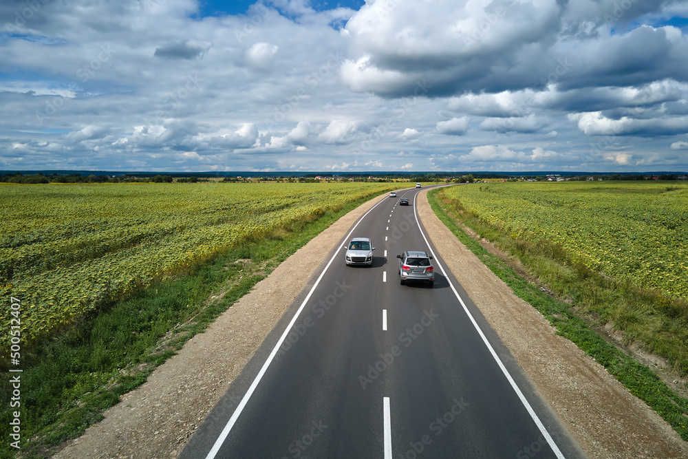 Aerial view of intercity road between green agricultural fields with fast driving cars. Top view from drone of highway traffic