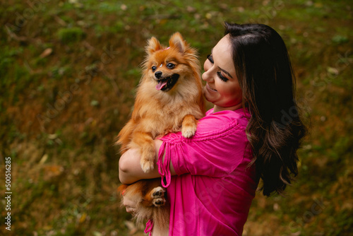 Woman with her pet dog on her lap. The Brazilian wearing a pink blouse and the dog with a bow on her head.