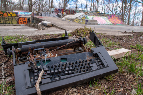 An old typewriter sits in the foreground of an abandoned skate park nestled in a forest at the top of a small cliff beside a section of the Bruce Trail that runs through Hamilton, Ontario. photo