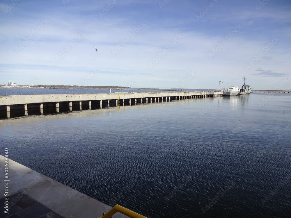 Obraz premium Seascape in early morning to stone pier with old boats moored. Ripple on navy water and blue sky. Noblessner, Tallinn, Estonia, Europe. April 2022