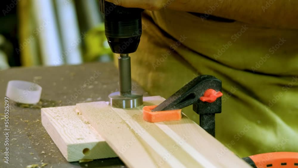 A mature male carpenter in the workshop creates a wooden product on a workbench A mature male carpenter in the workshop creates a wooden product on a workbench