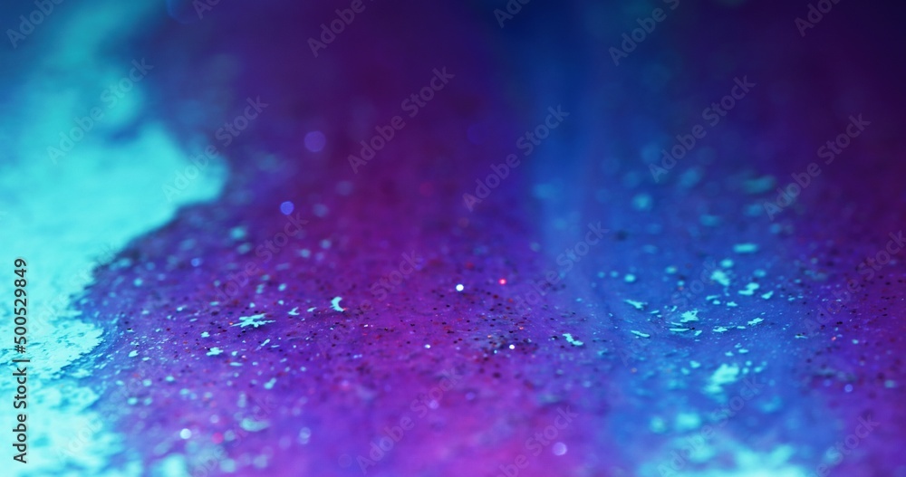 Fototapeta premium Glitter ink flow. Color fluid texture. Bokeh light. Defocused fluorescent purple pink blue shimmering particles paint abstract art background.