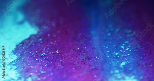 Glitter ink flow. Color fluid texture. Bokeh light. Defocused fluorescent purple pink blue shimmering particles paint abstract art background.