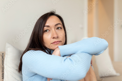 Fotobehang Frustrated Asian lady sitting on sofa, cuddling pillow, looking away at window
