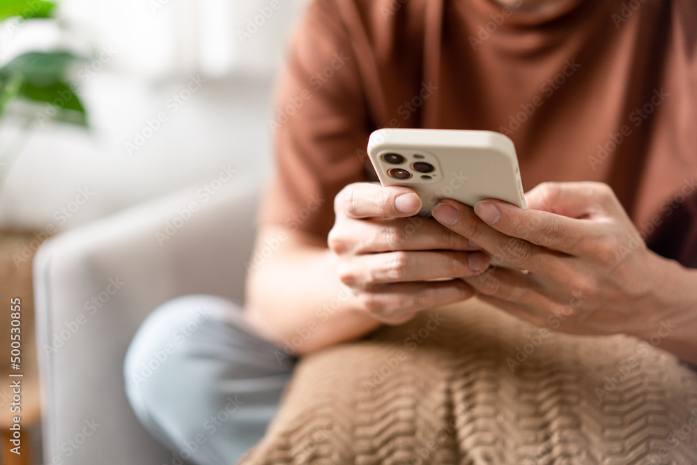 Technology Concept The man sitting next to a pot of plant, putting a small pillow on his lap, and checking something on his smartphone Technology Concept The man sitting next to a pot of plant, putting a small pillow on his lap, and checking something on his smartphone