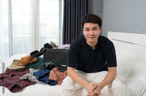 man preparing and packing clothes into suitcase on bed at home, holiday travel concept