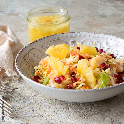 a bowl of coleslaw with pineapple and pomegranate on a light table photo