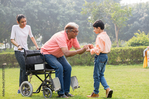 Photography Senior man trying to get up from wheelchair with the help of grandson and grandd
