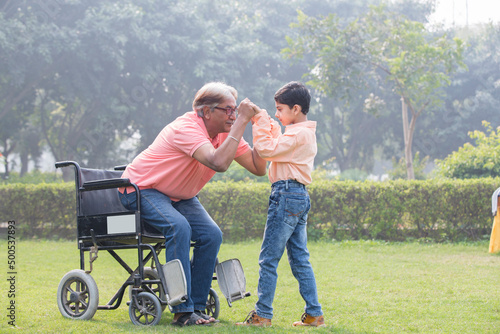 Senior man trying to get up from wheelchair with the help of grandson at park