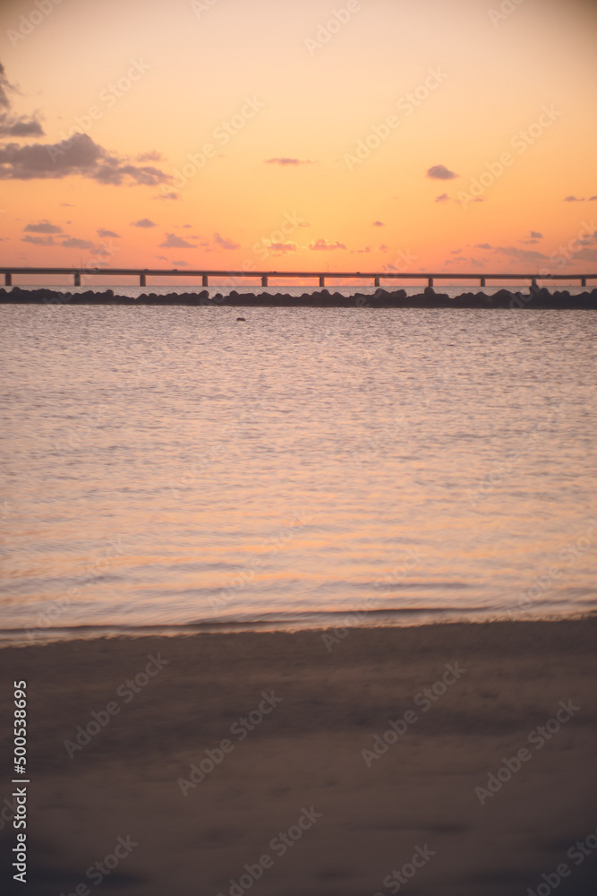 沖縄県の離島 宮古島の伊良部大橋に沈む赤い夕陽をトゥリバー海浜公園サンセットビーチから眺める