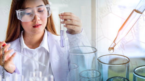 Attractive scientist woman looking chemical sample in flask at laboratory with lab glassware background. Science or chemistry research and development concept.