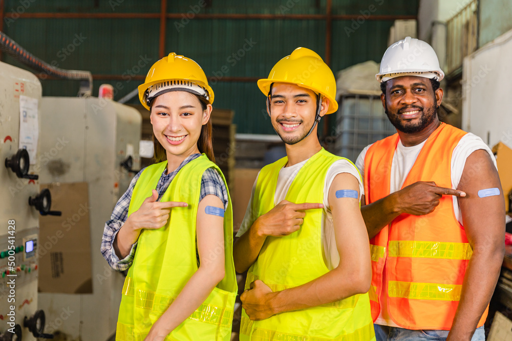 Asian young workers and African man pointing at his arm with a bandage after receiving the covid-19 vaccine.Vaccination for Essential Workers in healthcare at industrial factory. Asian young workers and African man pointing at his arm with a bandage after receiving the covid-19 vaccine.Vaccination for Essential Workers in healthcare at industrial factory.