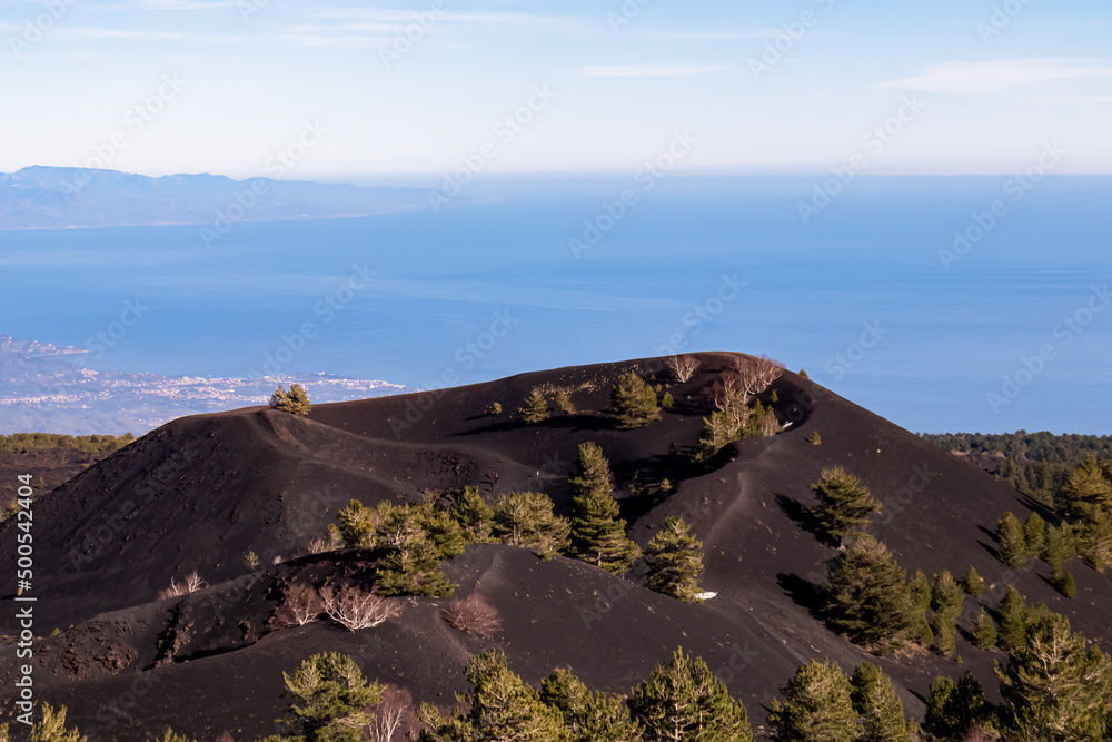 Solidified lava, ash, pumice fields on erupted Sartorio crater. Landscape with dark volcanic sand on bare terrain. Scenic view from volcano mount Etna, in Sicily, Italy, Europe. View on the Ionian sea
