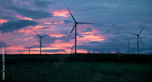 Wind farm or wind park, with high wind turbines in the setting sun for generation electricity with copy space. Green energy concept to reduce climate change and global warming