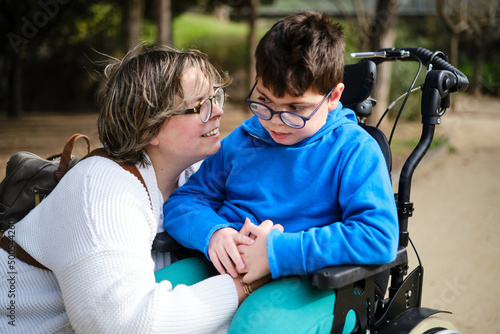 Foto Disabled boy in a wheelchair enjoying a walk outdoors with his mother