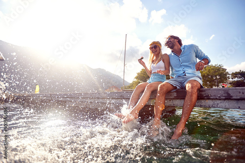 Fotografie, Obraz Attractive couple laughing while sitting on jetty near water