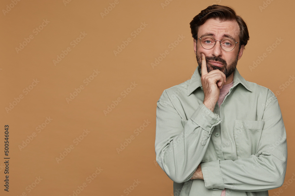 studio portrait of bearded man posing over beige background looking into camera with tired, bored facial expression studio portrait of bearded man posing over beige background looking into camera with tired, bored facial expression