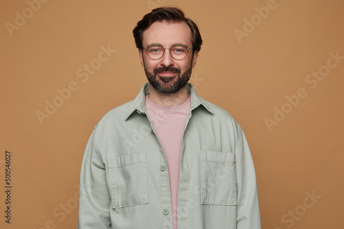 studio portrait of bearded man posing over beige background looking into camera with calm facial expression