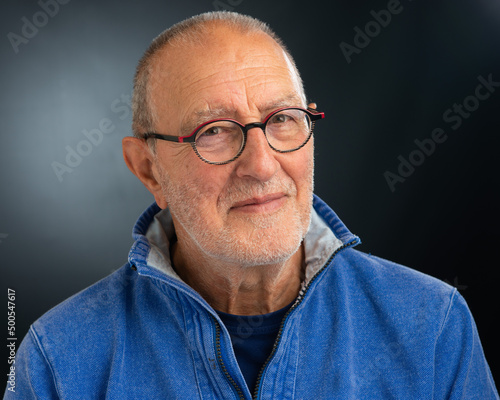 Close up portrait of a senior man in a blue top on a grey background with copy space