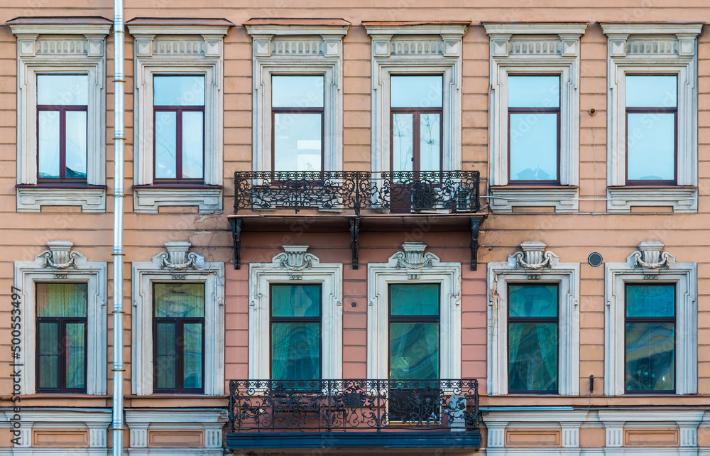 Fototapeta premium Two balconies and many windows in a row on the facade of the urban historic apartment building front view, Saint Petersburg, Russia 