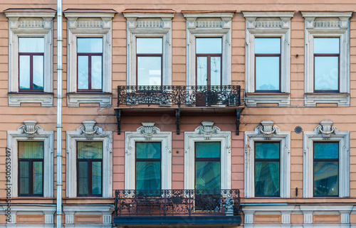 Two balconies and many windows in a row on the facade of the urban historic apartment building front view, Saint Petersburg, Russia
