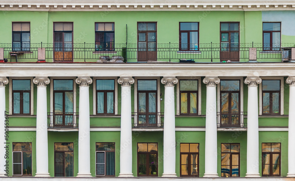 Balconies, columns and many windows in a row on the facade of the urban historic apartment building front view, Saint Petersburg, Russia
