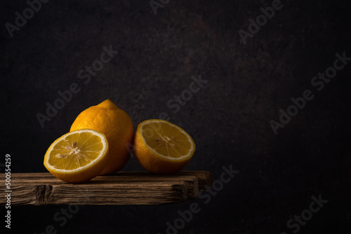 whole and halves of a fresh ripe lemon lie in a group on old boards on a dark soft background. side view. moody artistic photo with copy space