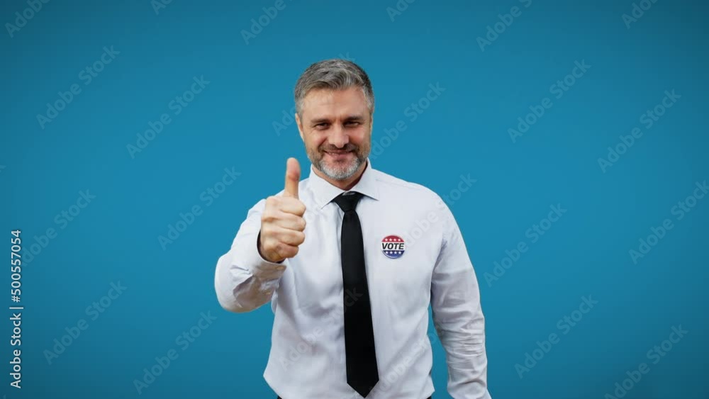 Happy male politician showing thumbs-up isolated on blue background, elections