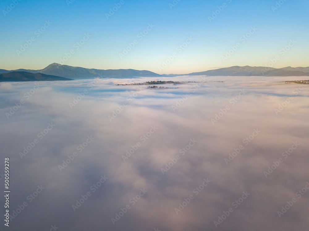 Flight over fog in Ukrainian Carpathians in summer. Mountains on the horizon. A thick layer of fog covers the mountains with a continuous carpet. Aerial drone view.