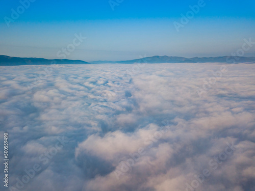 Flight over fog in Ukrainian Carpathians in summer. Mountains on the horizon. Aerial drone view.