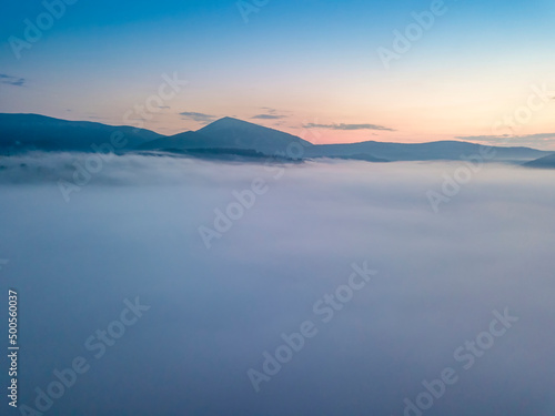 The rays of dawn over the fog in the Ukrainian Carpathians. Aerial drone view.