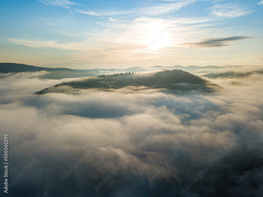 Sunny morning in the foggy Carpathians. A thin layer of fog covers the mountains. Aerial drone view.