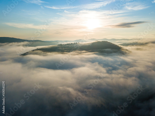 Sunny morning in the foggy Carpathians. A thin layer of fog covers the mountains. Aerial drone view. © Sergey