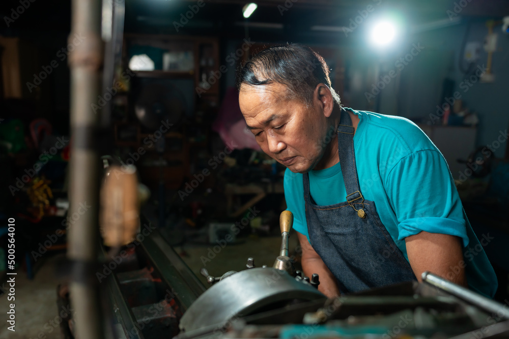 Portrait of Asian senior man working as a steel lathe is preparing work and equipment to turn steel and a small lathe in the family industry. Portrait of Asian senior man working as a steel lathe is preparing work and equipment to turn steel and a small lathe in the family industry.