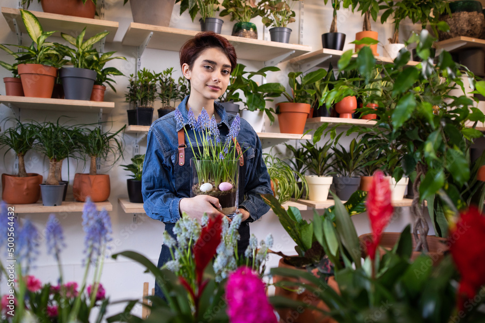 Portrait of smiling mid female florist carrying crate full of flower plants in shop