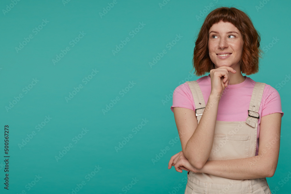 indoor portrait of young ginger female posing over blue background looking aside with thoughtfully facial expression indoor portrait of young ginger female posing over blue background looking aside with thoughtfully facial expression