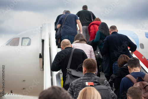 People climb the ramp to the plane. Passengers are loaded into the aircraft. People go up the stairs to the cabin of air transport.