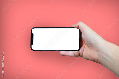 Hand holding the black smartphone with blank screen and modern frame less design on pink colour background