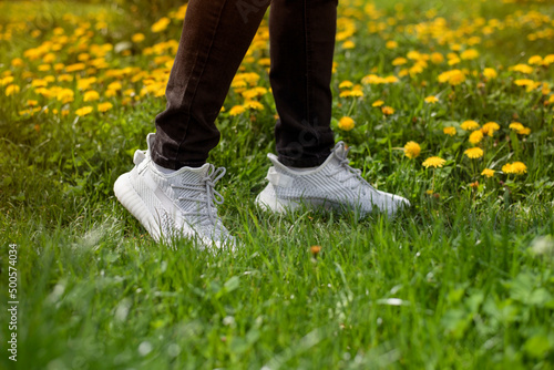The young man returns from the store where he bought new fabric sneakers and immediately puts them on. Bright sports shoes made of fabric on the feet of a guy walking on the grass