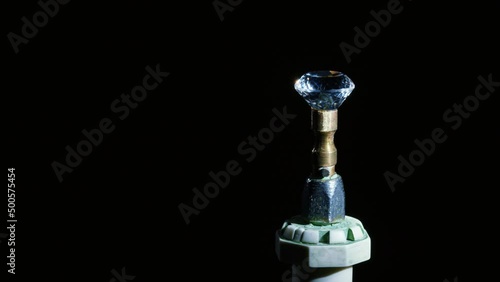 Transparent gemstone turns on metal dop stick, sparkles after processing on black. Precious gem after jewelry cutting is visible from different angles on dopstick. Diamond, rhinestone, topaz photo