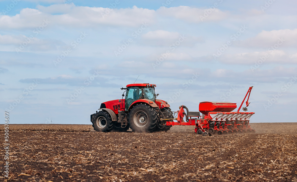 Obraz premium Spring sowing season. Farmer with a tractor sows corn seeds on his field. Planting corn with trailed planter. Farming seeding. The concept of agriculture and agricultural machinery.
