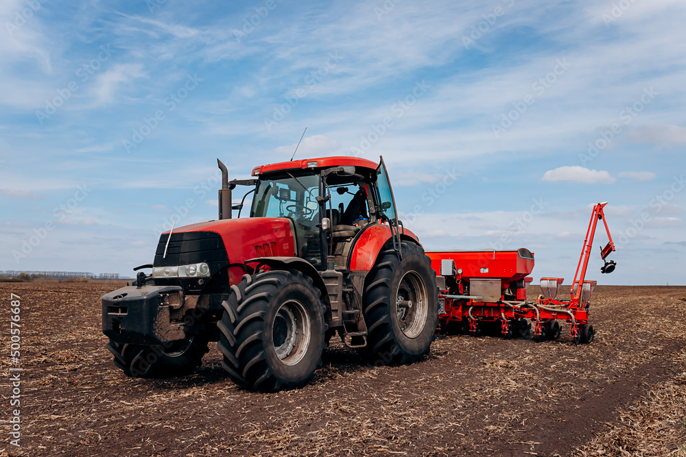 Spring sowing season. Farmer with a tractor sows corn seeds on his field. Planting corn with trailed planter. Farming seeding. The concept of agriculture and agricultural machinery. Spring sowing season. Farmer with a tractor sows corn seeds on his field. Planting corn with trailed planter. Farming seeding. The concept of agriculture and agricultural machinery.