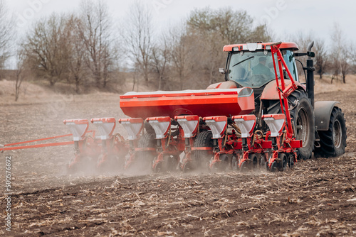 Spring sowing season. Farmer with a tractor sows corn seeds on his field. Planting corn with trailed planter. Farming seeding. The concept of agriculture and agricultural machinery. photo