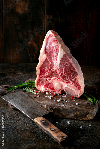 Large raw t-bone steak on a wooden board with seasonings and pepper. Florentine or Porterhouse steak with a meat cleaver photo